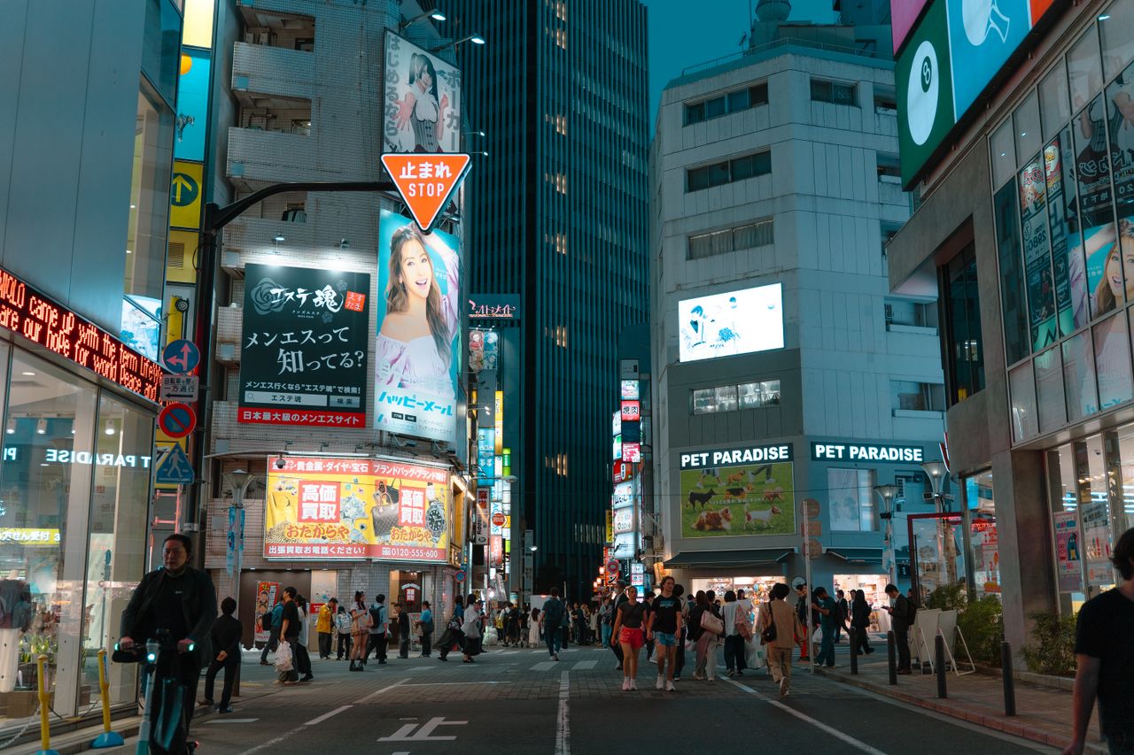 Vue nocturne saisissante d'une rue animée de Tokyo, remplie de lumières et de passants.
